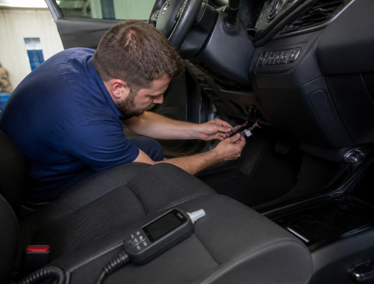 Technician wiring a BAIID breathalyzer ignition interlock device under a car dashboard